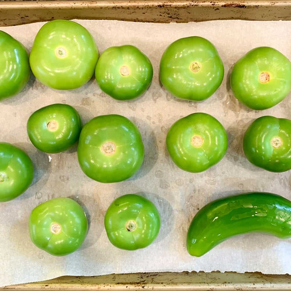 Tomatillos and jalapeno on a parchment lined baking sheet.