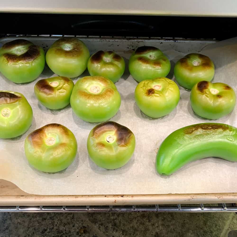 Tomatillos and jalapeno on a parchment lined baking sheet coming out of the broiler blistered.
