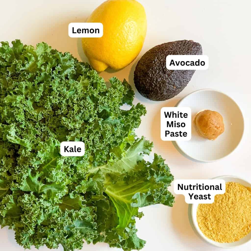 Ingredients for avocado and kale salad - fresh curly kale, lemon, miso paste, nutritional yeast and avocado.