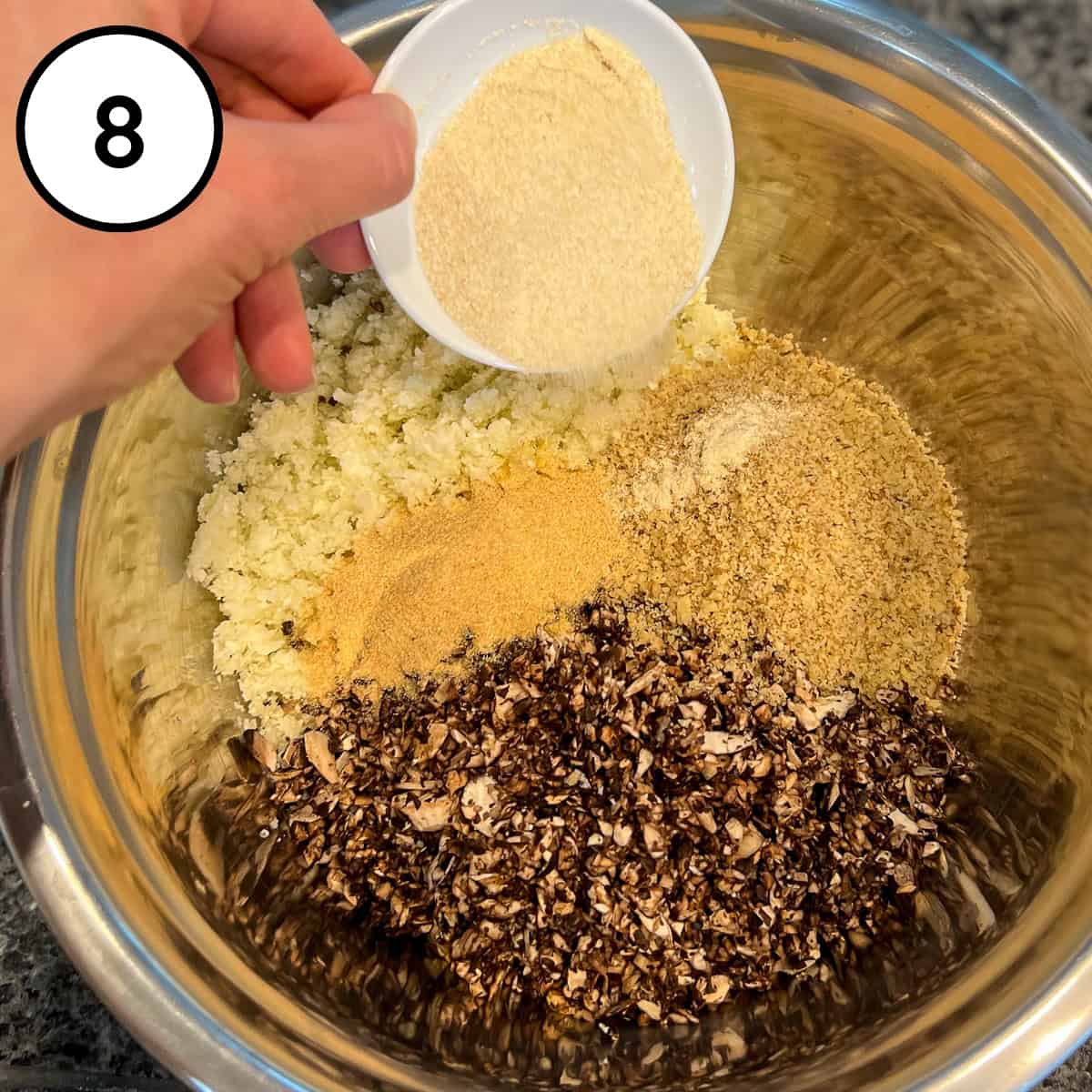 Garlic powder and onion powder being added to the mixing bowl with processed mushrooms, walnuts and cauliflower.