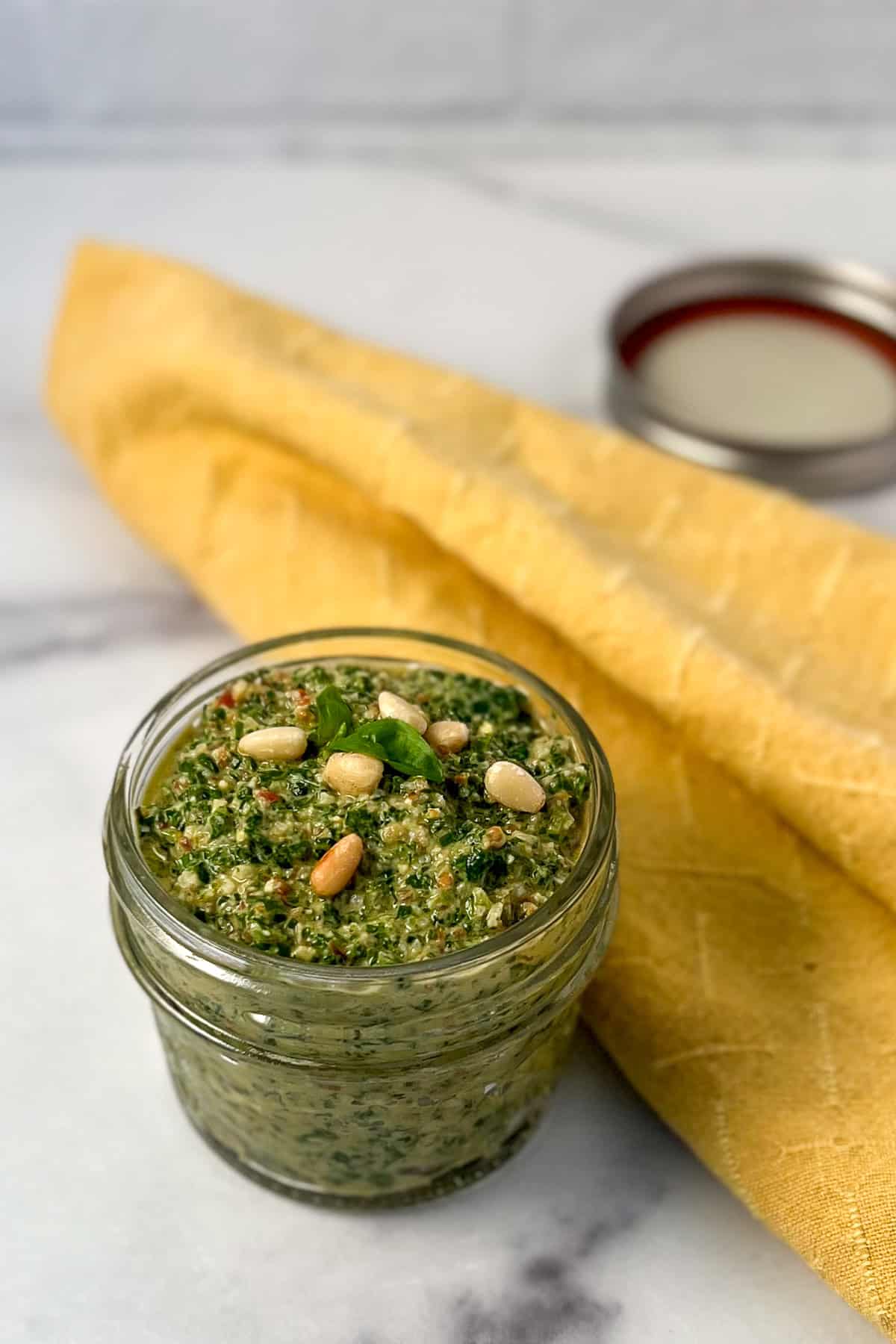 Arugula Basil Pesto in a small mason jar topped with toasted pine nuts and fresh basil leaves.