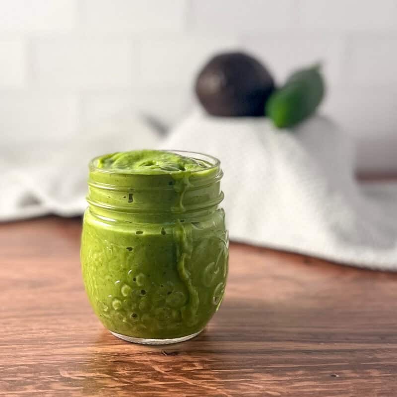 Avocado cilantro lime dressing in a mason jar; avocado and jalapeno blurred in the background.