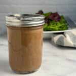 side view close up of a mason jar with balsamic vinaigrette dressing and mixed greens salad blurred in the background
