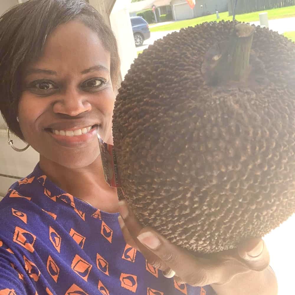 Sersie smiling while she's holding a brown ripened jackfruit to be used in the sweet and sassy jackfruit salsa.