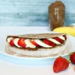 Chocolate hummus breakfast wrap on a plate with strawberries and banana on the side.