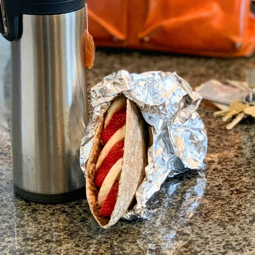 Chocolate hummus wrap wrapped in foil with coffee thermos and keys on the side.