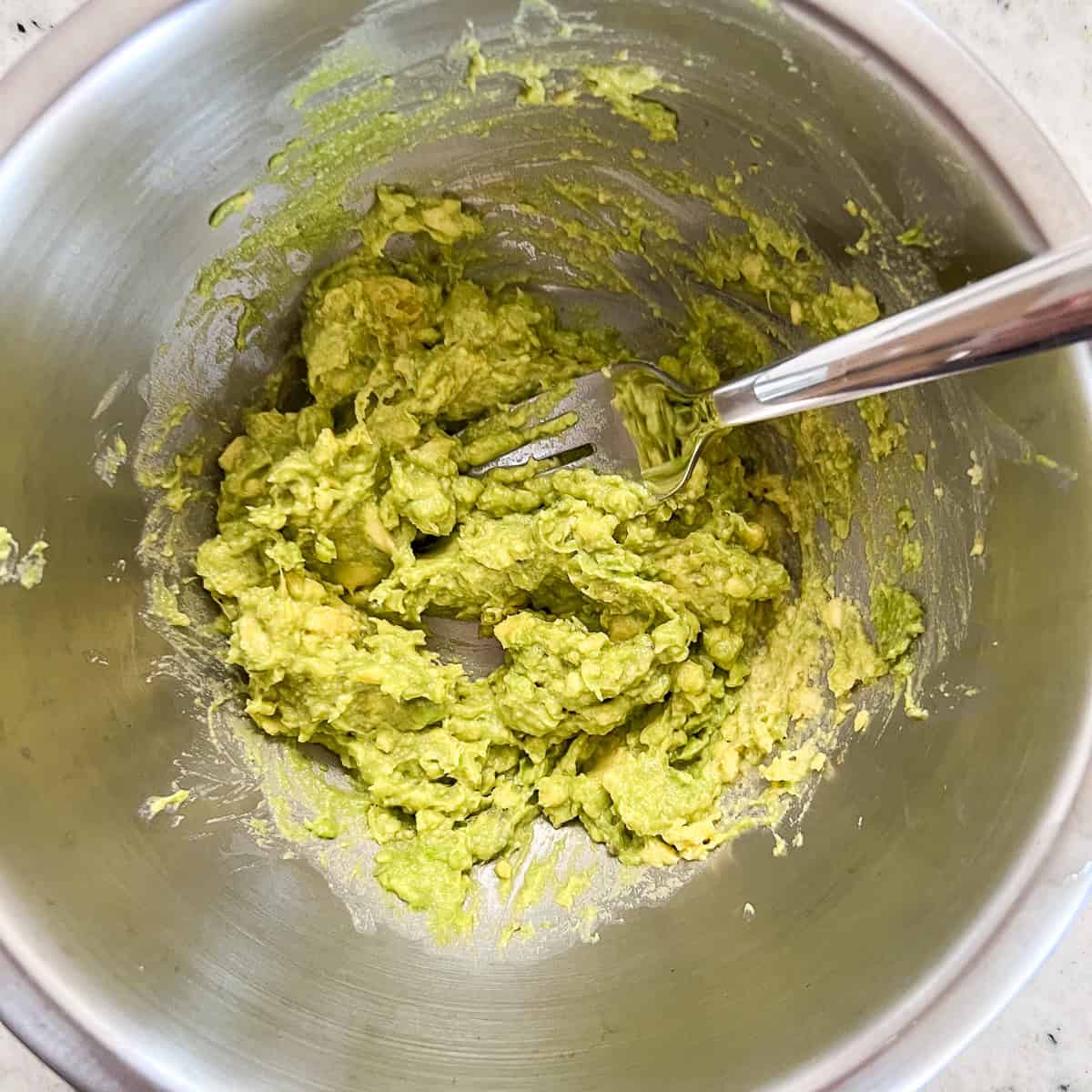 Avocado being mashed in a small mixing bowl with a fork.