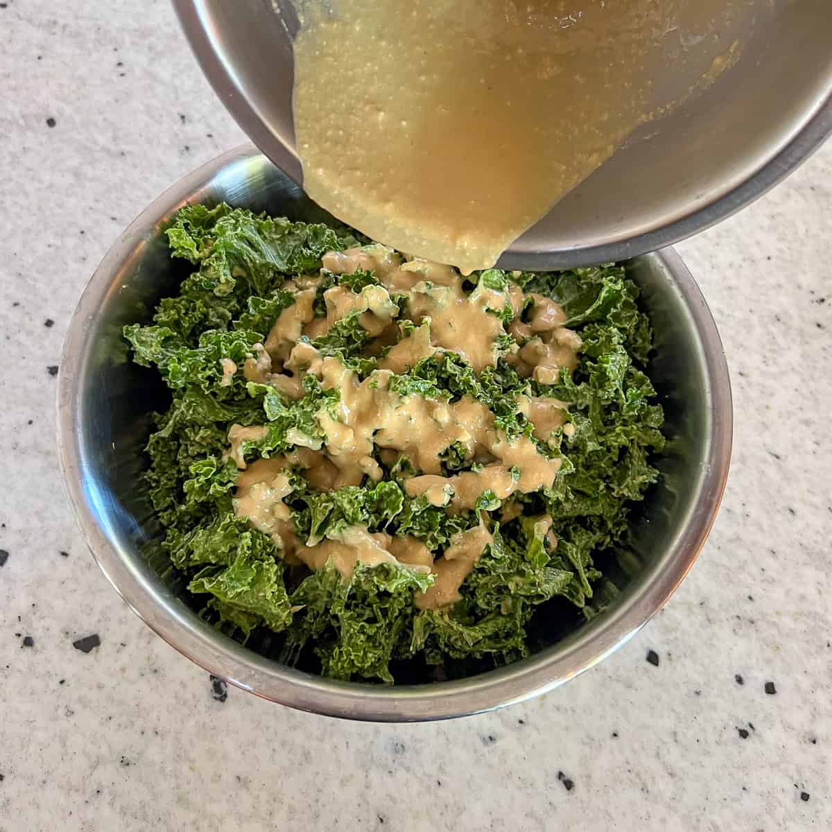 Dressing being poured over the kale and avocado salad in a mixing bowl.