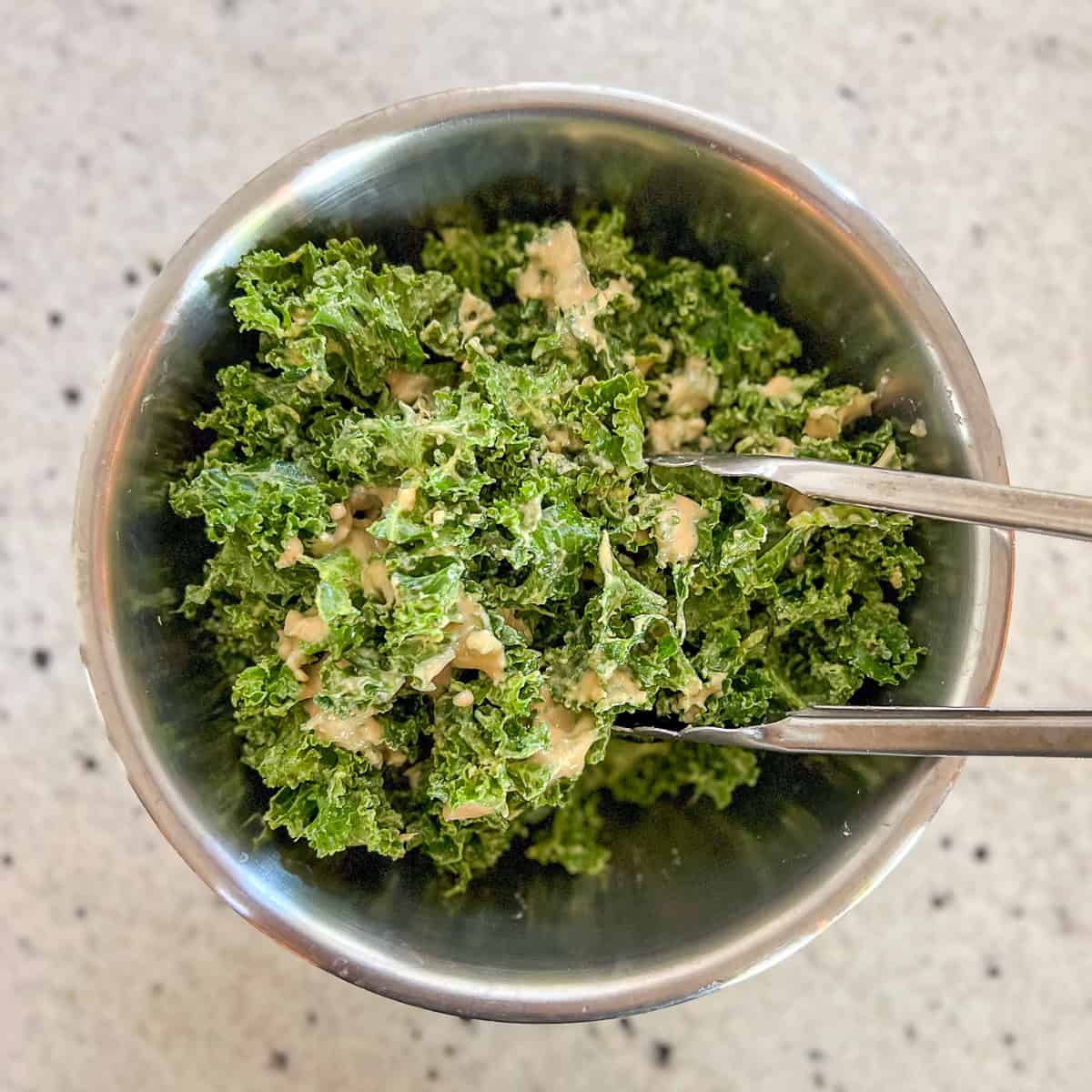Tongs being used to toss the salad in a mixing bowl.
