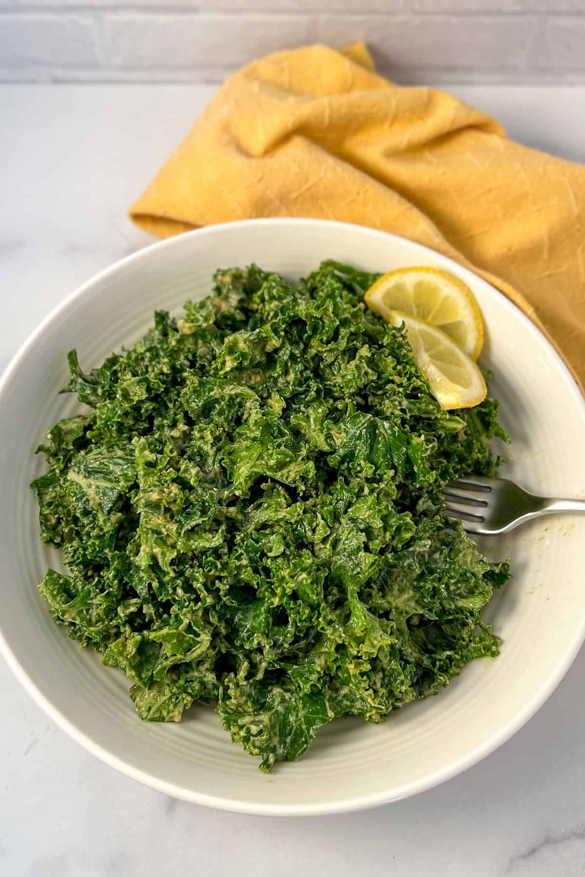 Kale and avocado salad in a bowl with a few slices of fresh lemon.