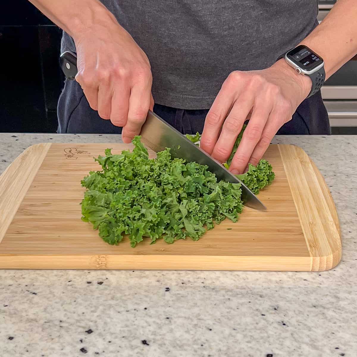 A woman chopping kale on a wooden cutting board.