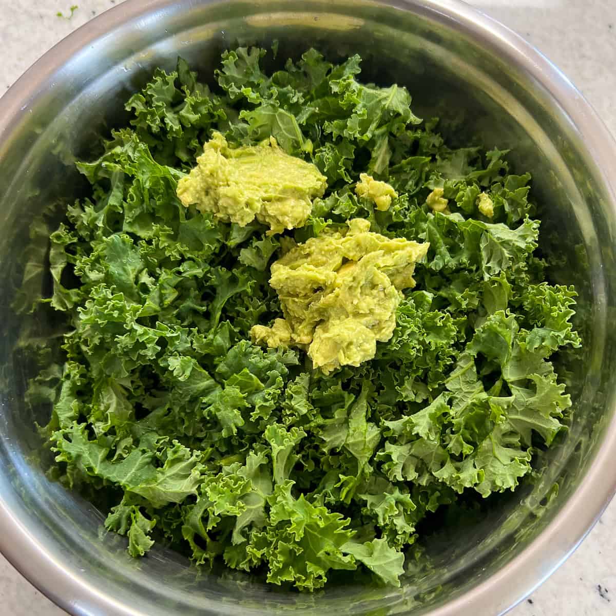 Mashed avocado added to the chopped kale in a large mixing bowl.