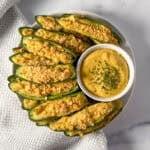 A plate of vegan jalapeno poppers with extra cashew cheese sauce on the side.
