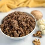 top side close up of vegan walnut meat in a white bowl with loose walnut pieces, cauliflower and mushroom on the side