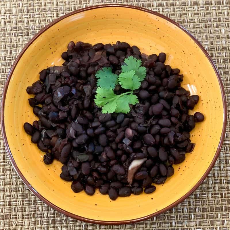 top view close up of easy cuban black beans in a yellow bowl with a sprig of fresh cilantro