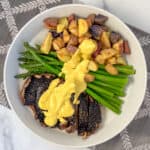 Portobello steaks with veggies covered in vegan béarnaise sauce, on a plate.