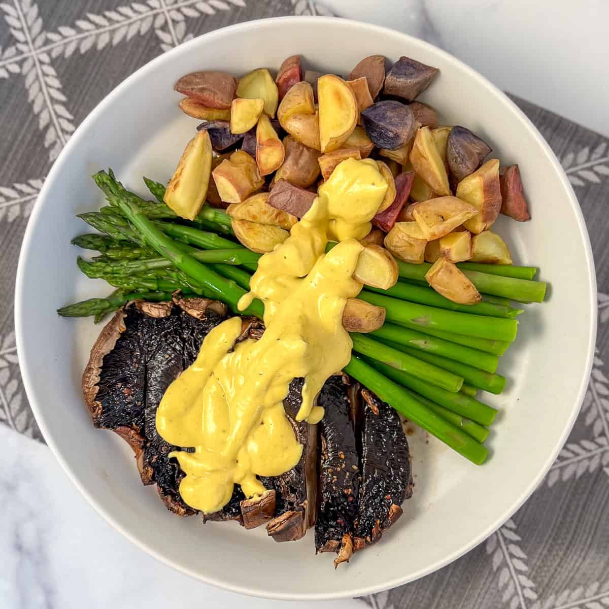 Portobello steaks with veggies covered in vegan béarnaise sauce, on a plate.