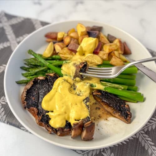 Portobello steaks with vegetables topped with vegan béarnaise sauce, and a fork with a bite.