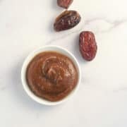 top view close up of homemade date syrup in a small white bowlwith loose dates next to it