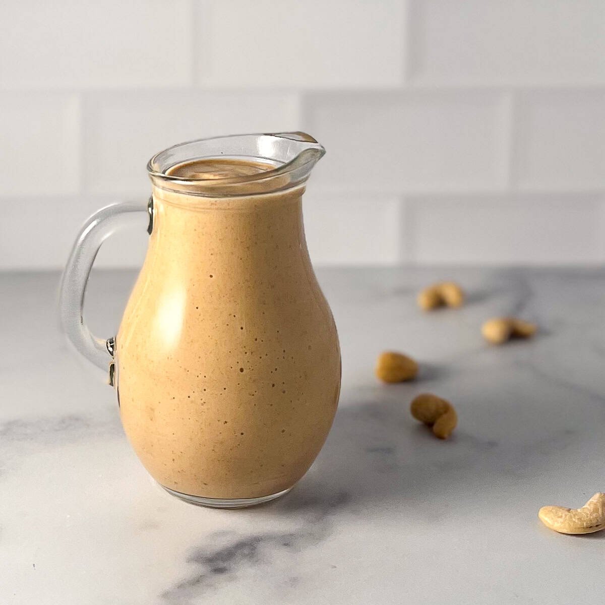 Spicy chipotle cream sauce in a small pitcher with loose cashews in the background.