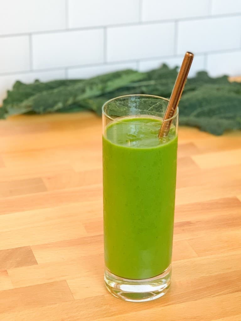 side view close up of Refreshing Kale Pineapple Avocado smoothie in a tall glass with metal straw