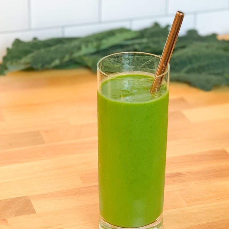 side view close up of Refreshing Kale Pineapple Smoothie in a tall glass with metal straw