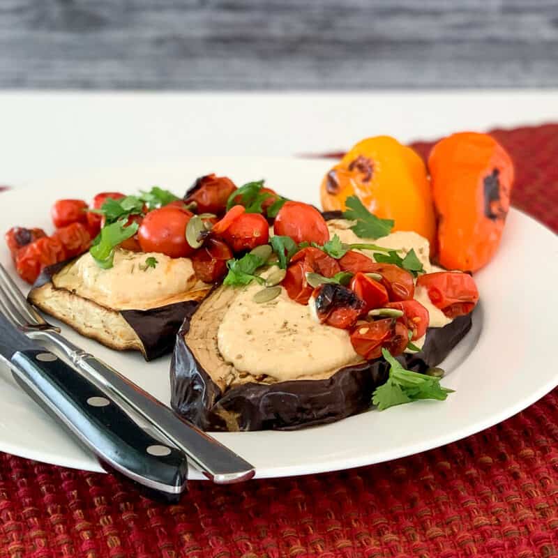 top side view of two grilled eggplant steaks topped with hummus, tomatoes and herbs