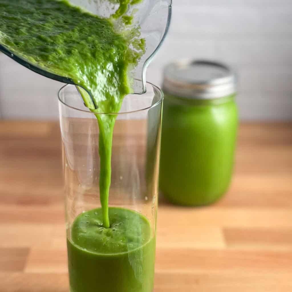 Kale pineapple smoothie being poured into a glass. Another smoothie in a mason jar in the background.