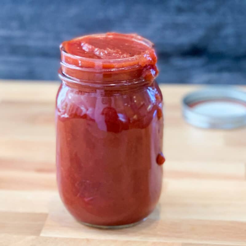 side view of vegan bbq sauce in a mason jar with some of the sauce dripping down the side; lid blurred in the background