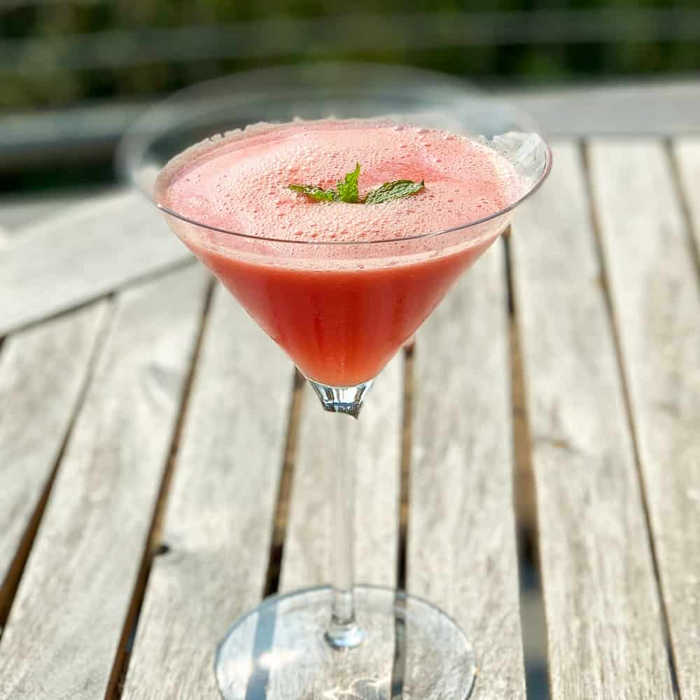 side view close up of watermelon mint mocktail in a martini glass sitting on wooden patio table