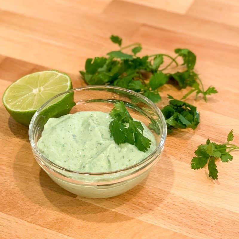 Cilantro Lime Ranch Dressing in a glass bowl next to a half of lime and some fresh cilantro on wooden surface