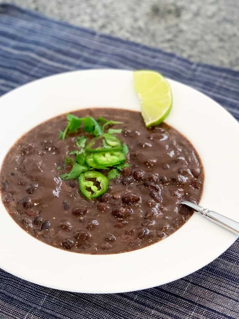 top view close up of 7-Minute Quick and Easy Black Bean Soup topped with fresh cilantro, jalapeno slices and lime wedge in a white bowl on dark blue placemat