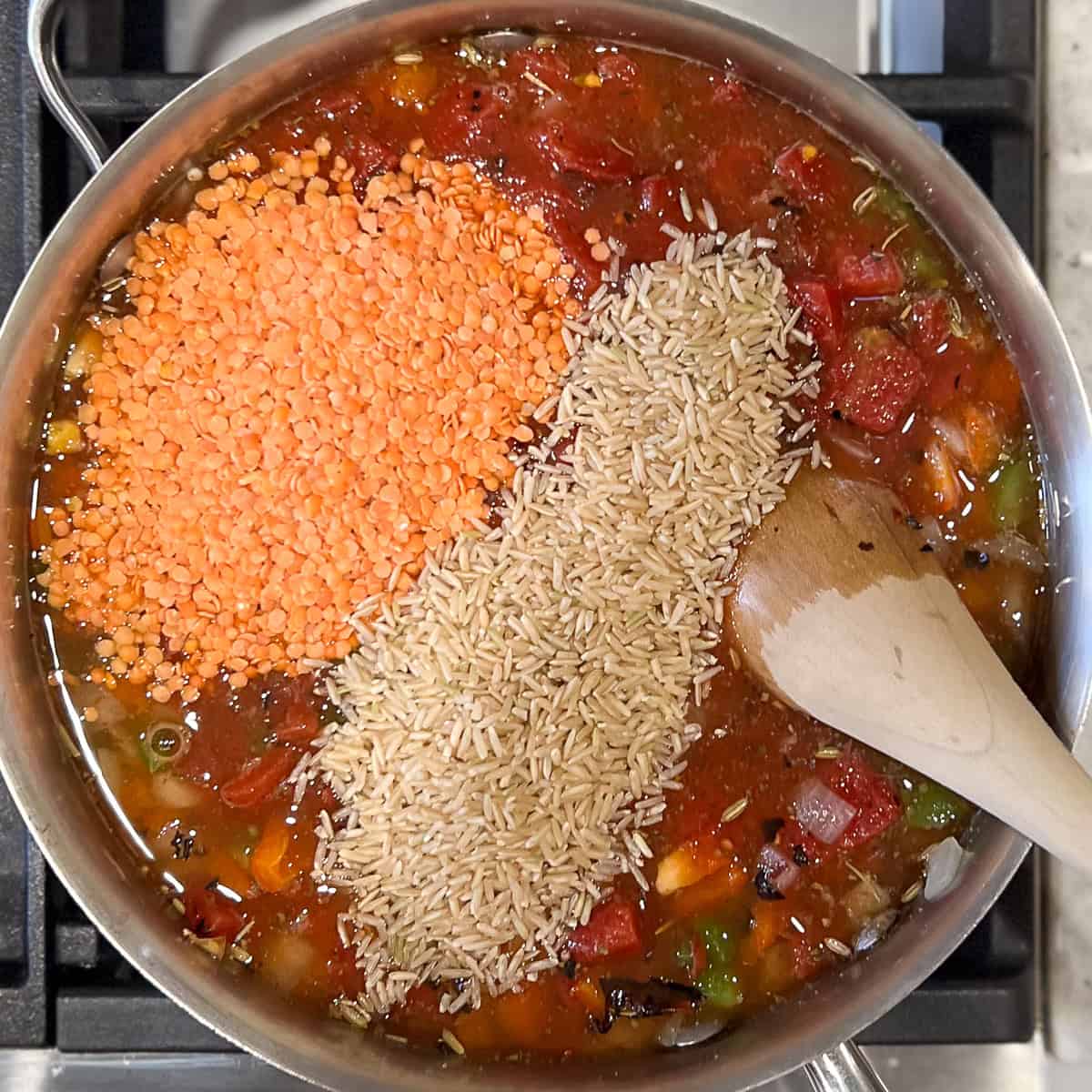 Lentils and brown rice added to the pan with other ingredients. Wooden spoon to stir everything.