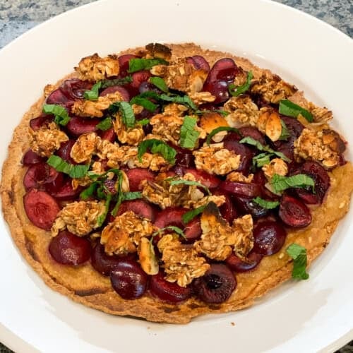 top side view close up of cherry oat fruit pizza on a white plate with oat crumbles and fresh mint