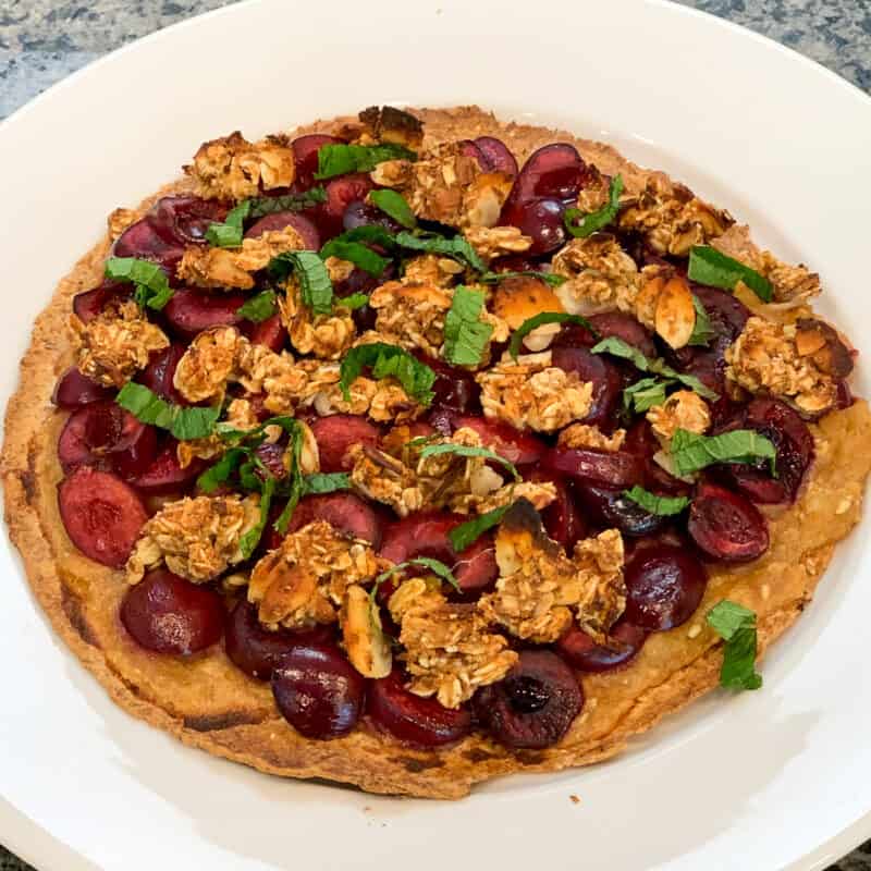 top side view close up of cherry oat fruit pizza on a white plate with oat crumbles and fresh mint