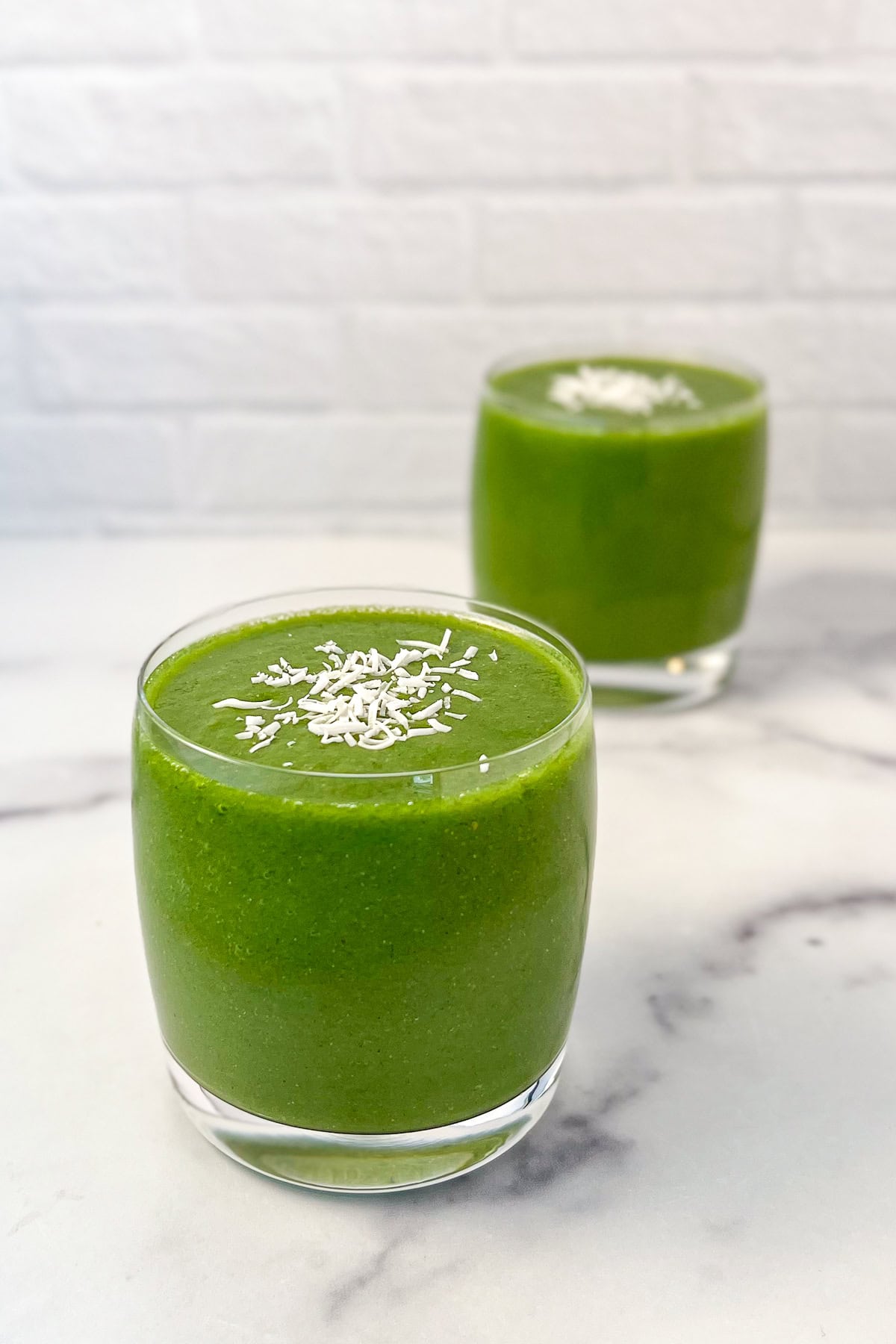Two glasses of pear and kale smoothie topped with shredded coconut flakes.