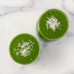 Two pear and kale smoothies with unsweetened coconut flakes on top.