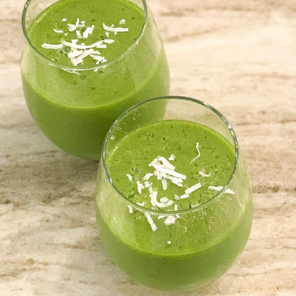top side view of two pear and kale smoothies in glass with sprinkled coconut flakes on top