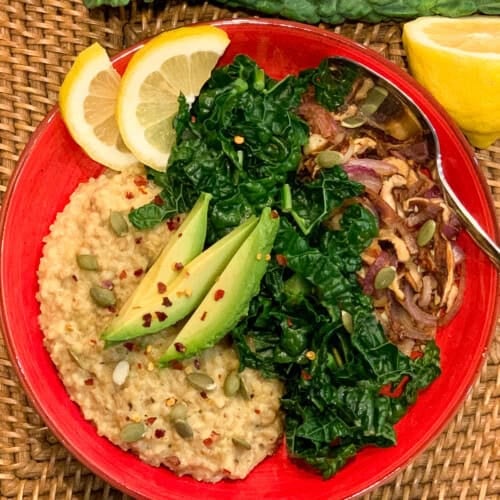 Bowl of steel cut oats with steamed kale and mushrooms, topped with avocado slices.