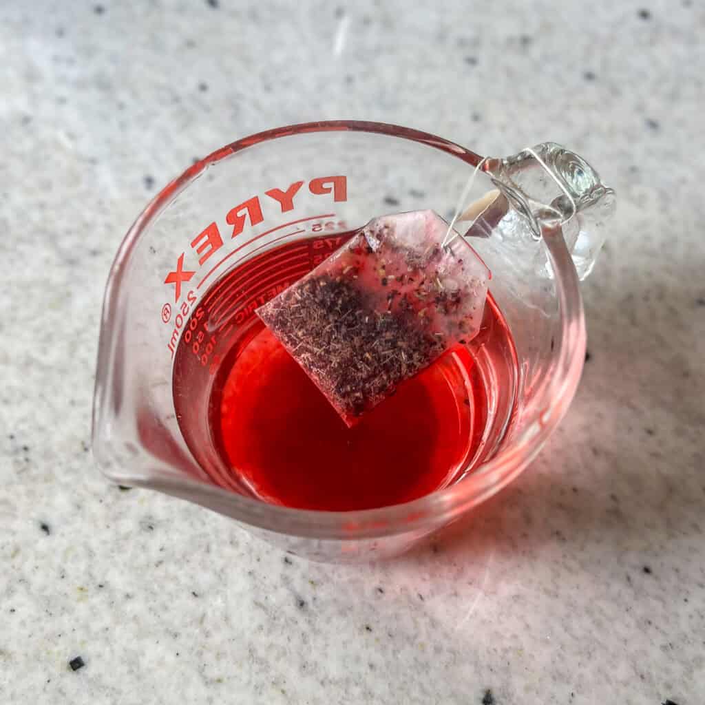 Tea steeping in hot water in a measuring cup.
