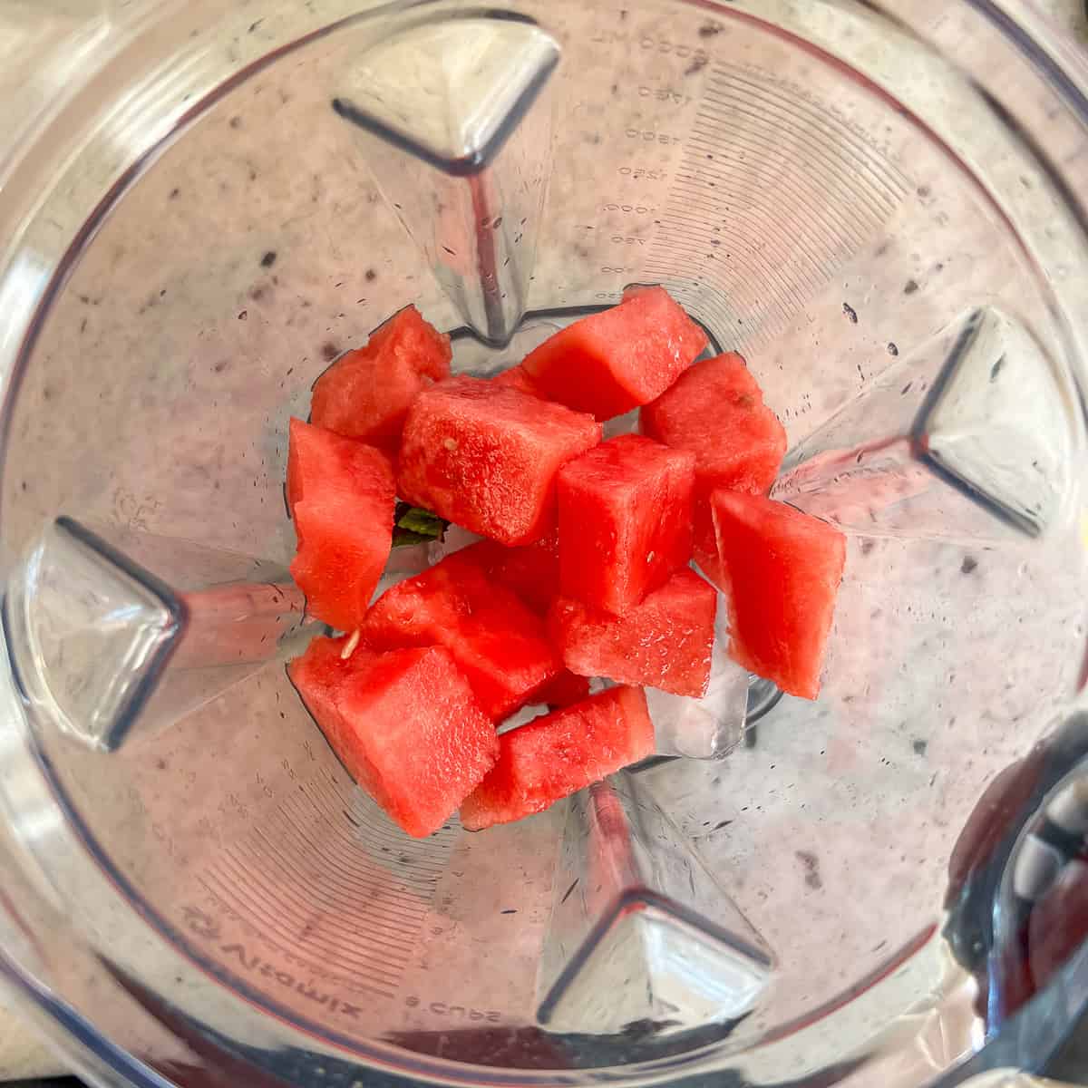 Watermelon, coconut water, lime juice, ice and a mint leaf in the pitcher of a high speed blender before blending.
