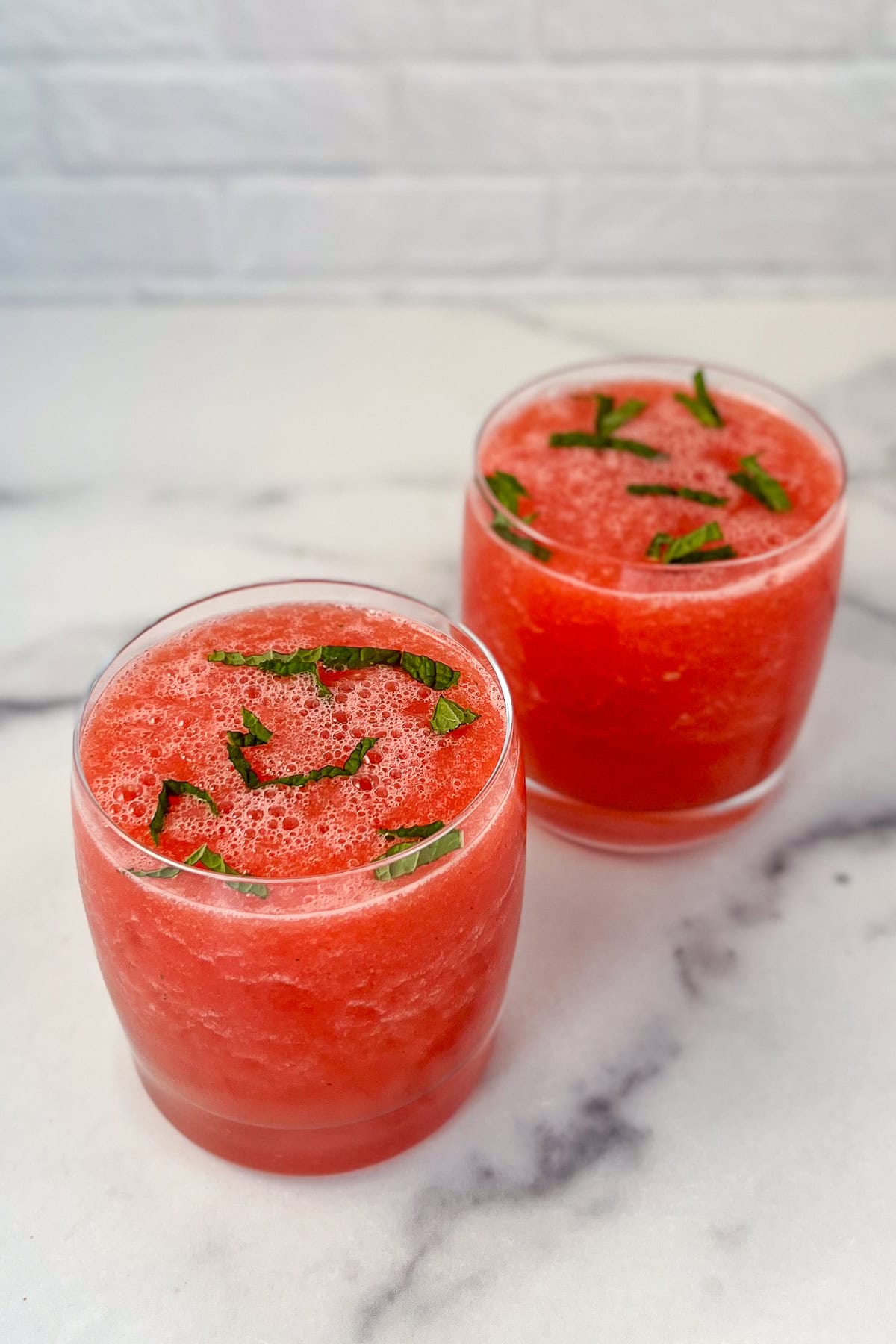 Two watermelon mint mocktails with finely chopped mint on top.