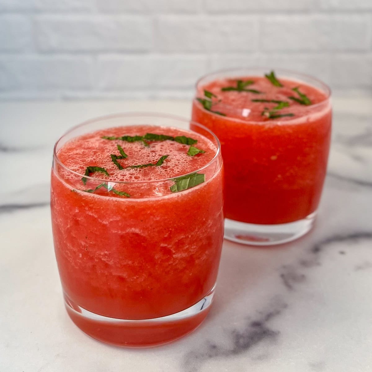 Two watermelon mint mocktails with finely chopped fresh mint on top.