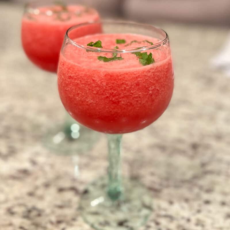side view of two stemmed glasses of watermelon mint mocktail on granite countertop