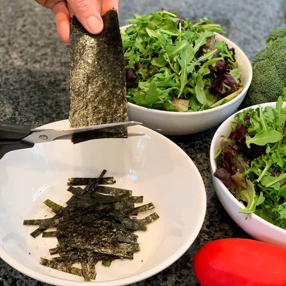 cutting nori seaweed sheets into strips with kitchen scissors for sushi salad with Creamy Tahini Ginger Dressing