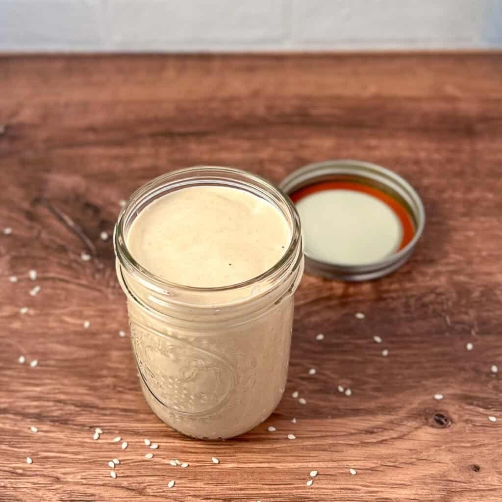 Creamy tahini ginger dressing in a mason jar with lid on the side.