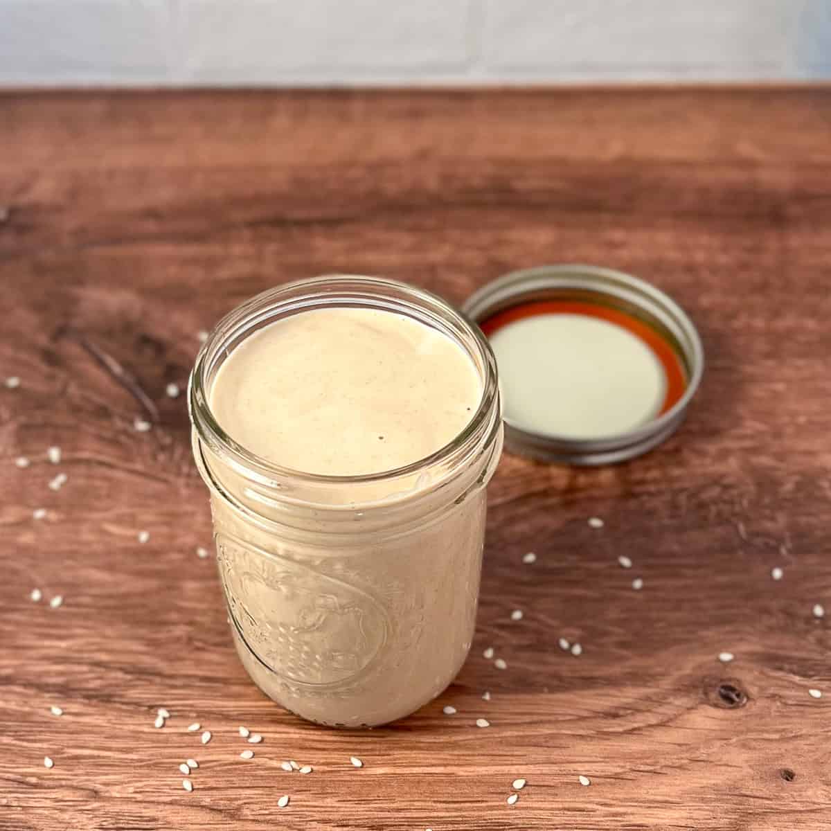 Creamy tahini ginger dressing in a mason jar with lid on the side.
