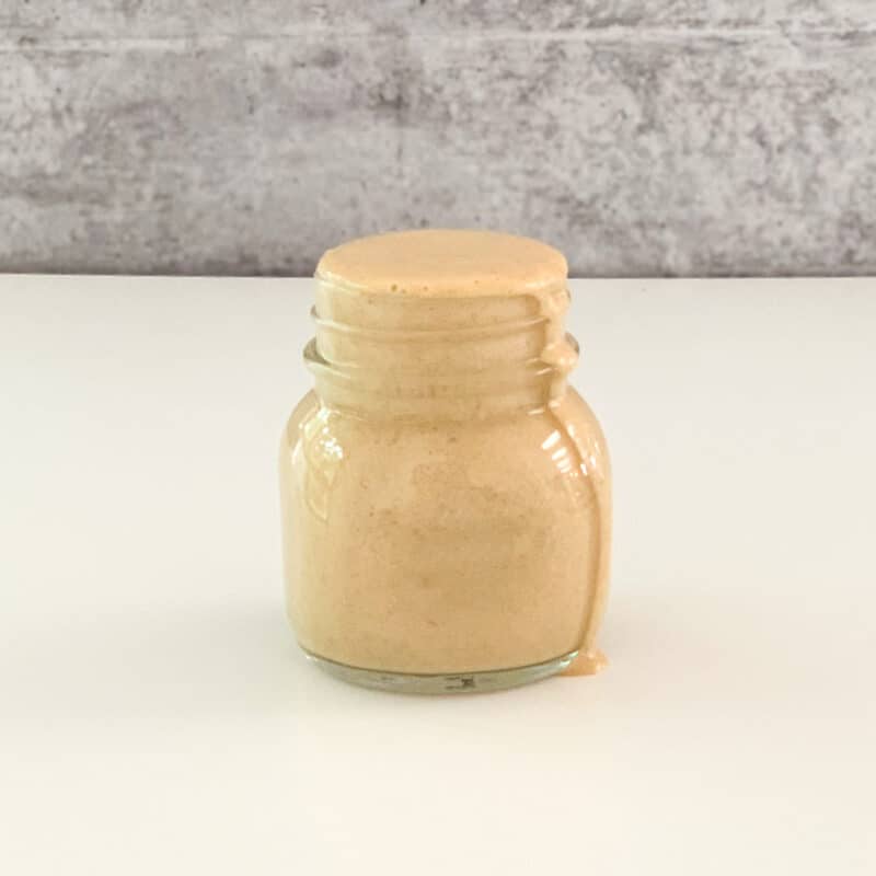side view of creamy tahini ginger dressing in a glass jar on a white surface