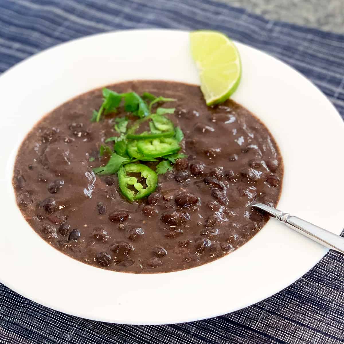 top side view of quick and easy black bean soup in a white rimmed bowl with fresh jalapeno and cilantro on top, and lime wedge on the side