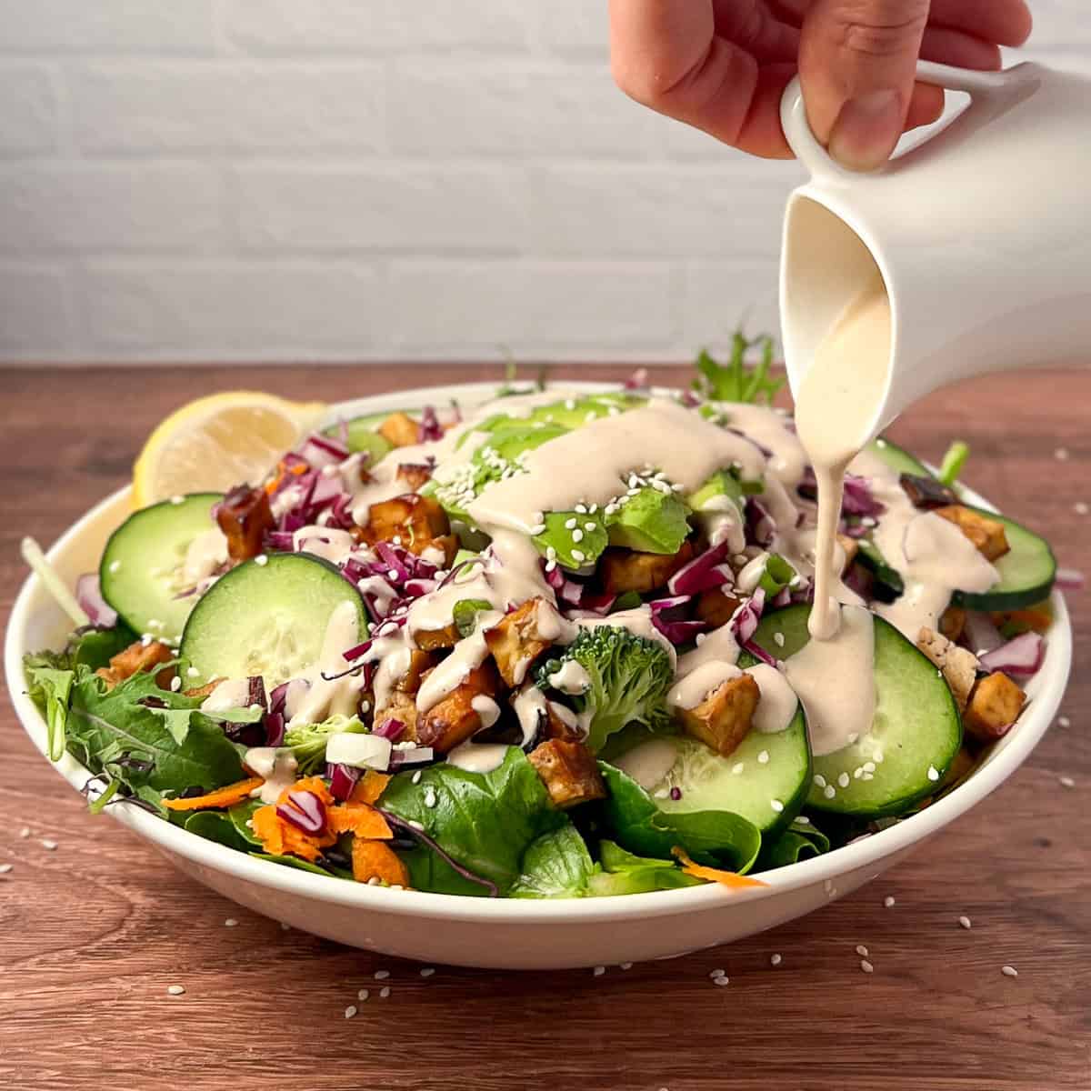Sushi salad in a bowl being topped with creamy tahini ginger dressing.